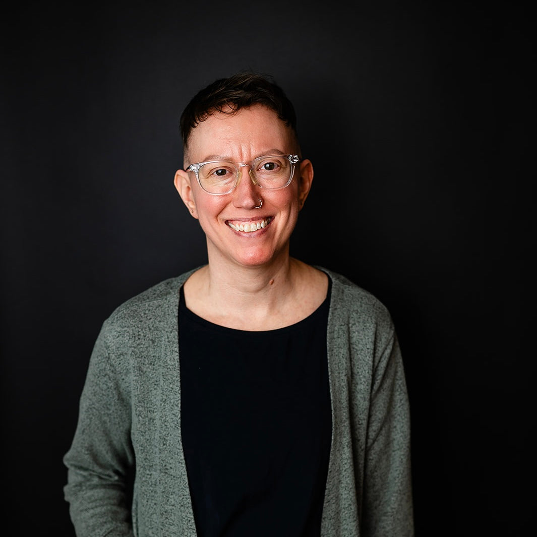 Founder, Vicki, wearing glasses and a gray cardigan over a black shirt against a dark background