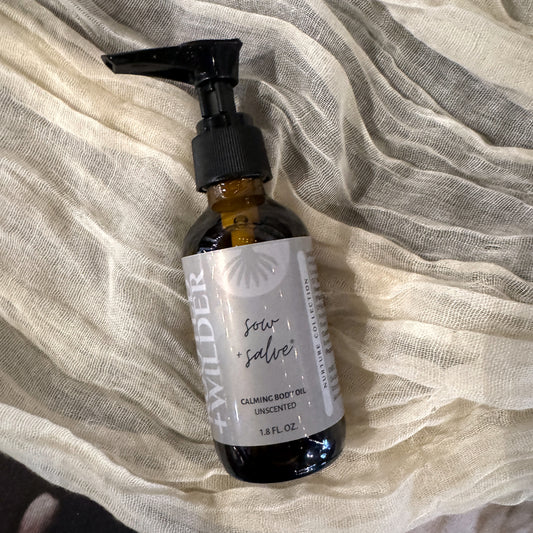 Bottle of Rooted+Wilder Calming Body Oil on a textured fabric background